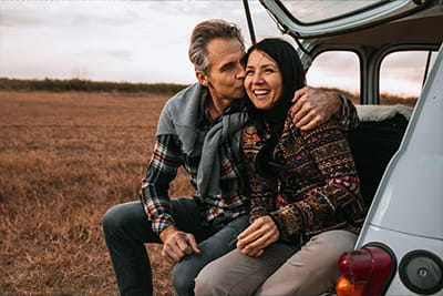 A couple sitting on the tailgate of a car in a grass field