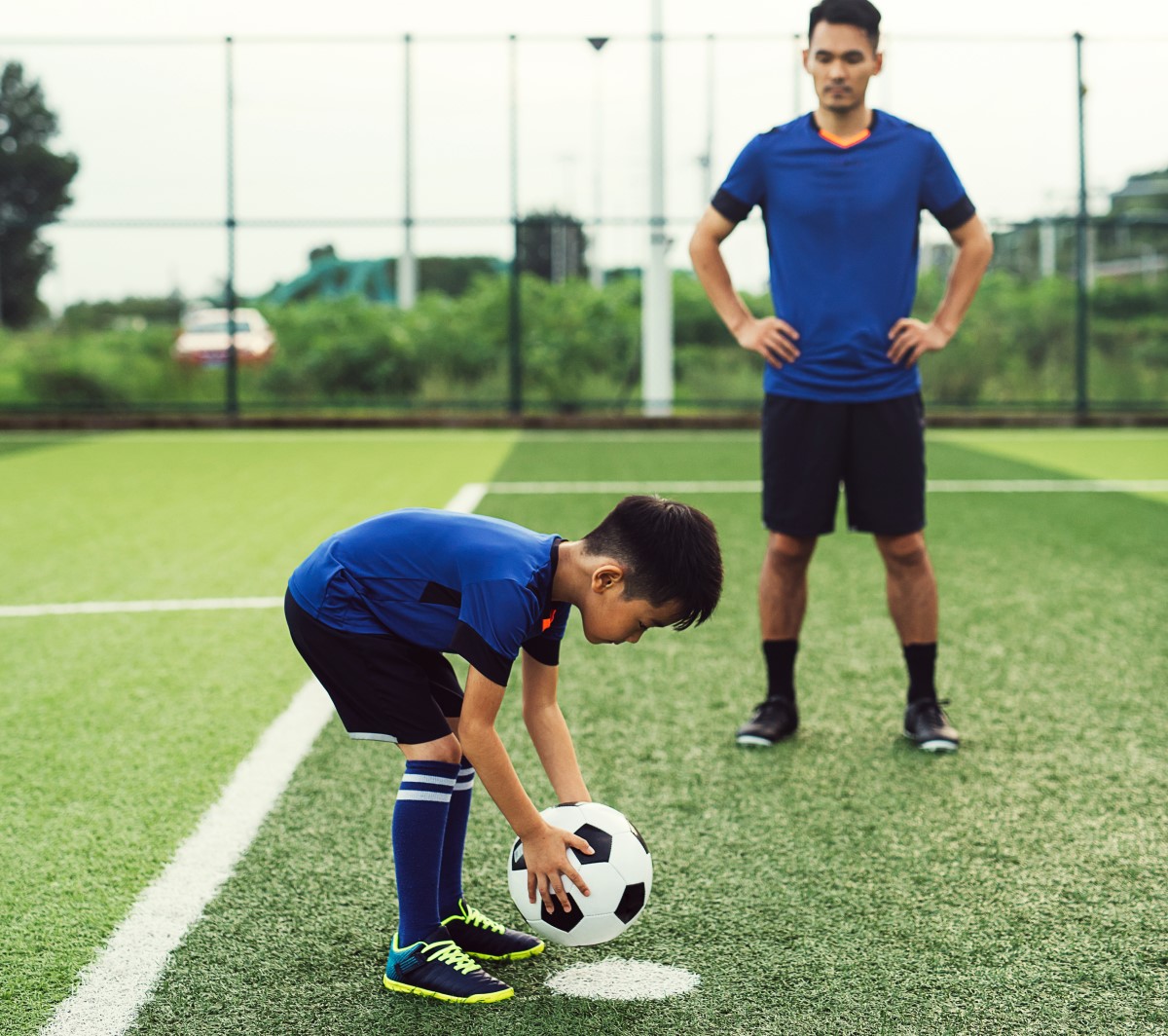 Young boy practising penalty kick as dad watches