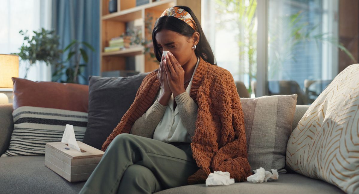 A women sitting on a couch, blowing her nose surrounded by tissues