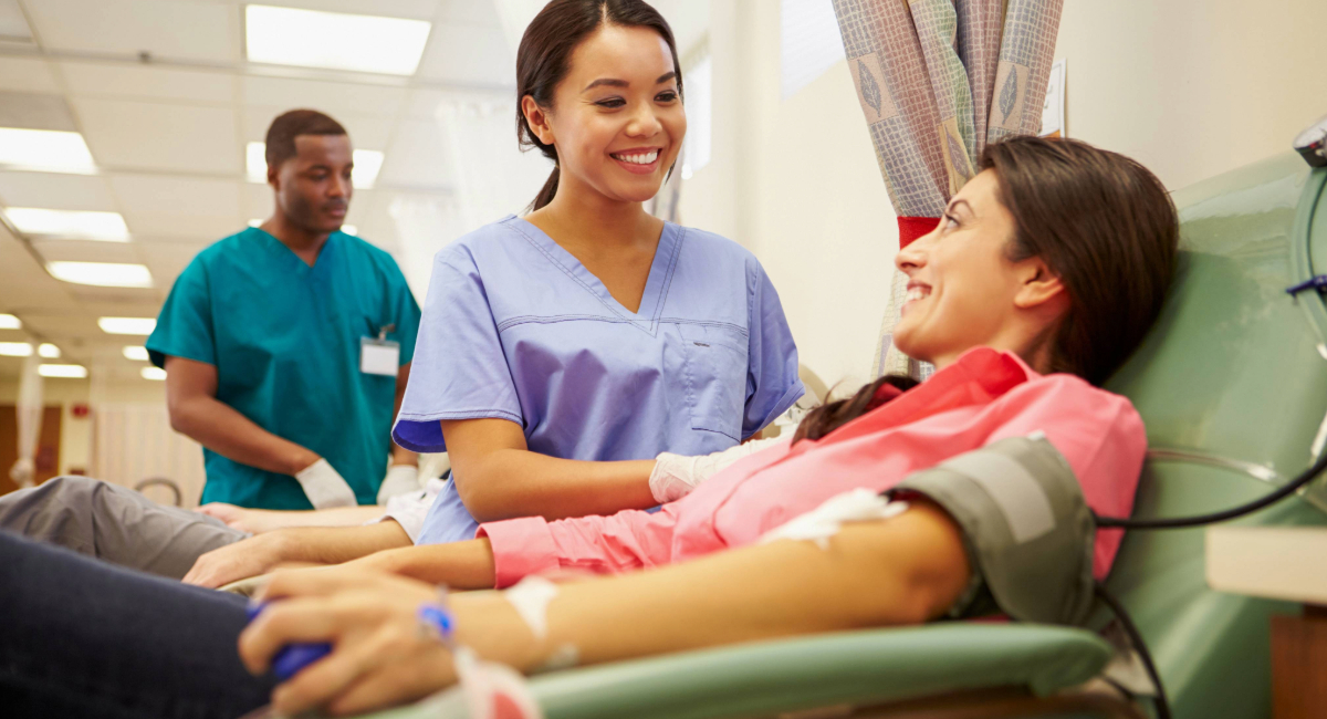 A woman smiling up at a nurse who is taking her blood