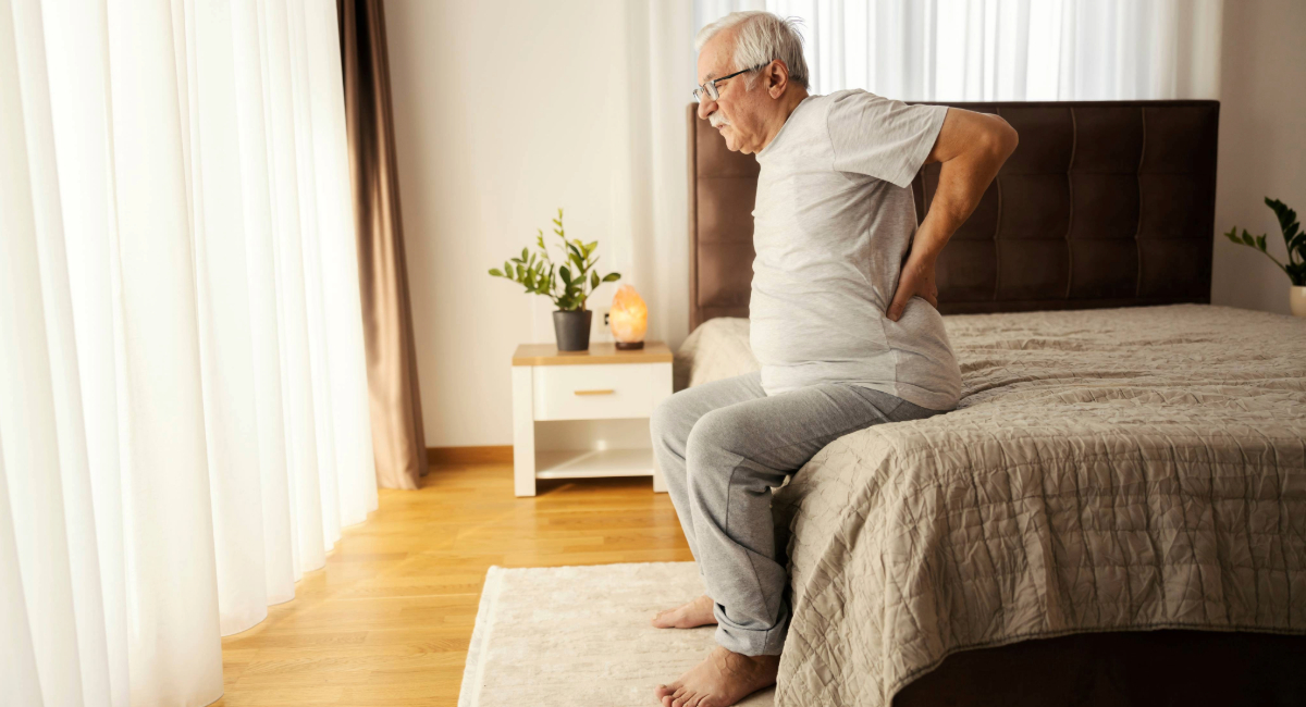 An older man sitting in bed holding his back