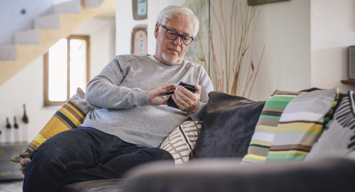 An older man sitting on the couch looking at his phone