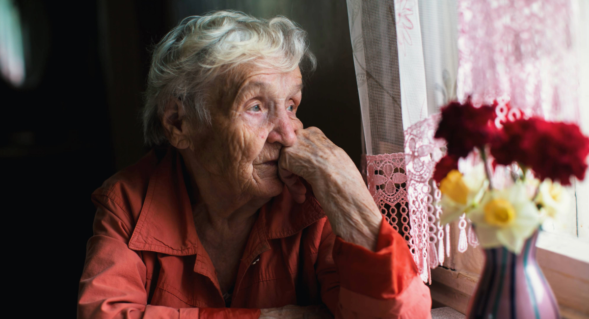 An elderly woman looking out the window depressed