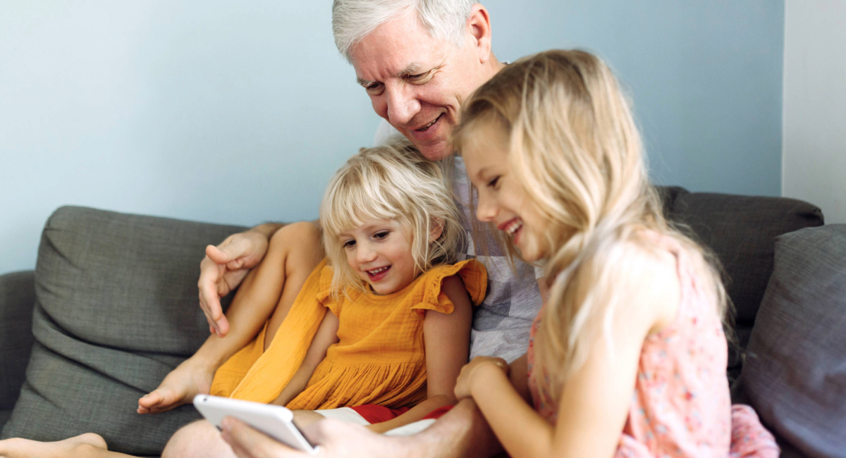 An older man reading a book to his two grand daughters