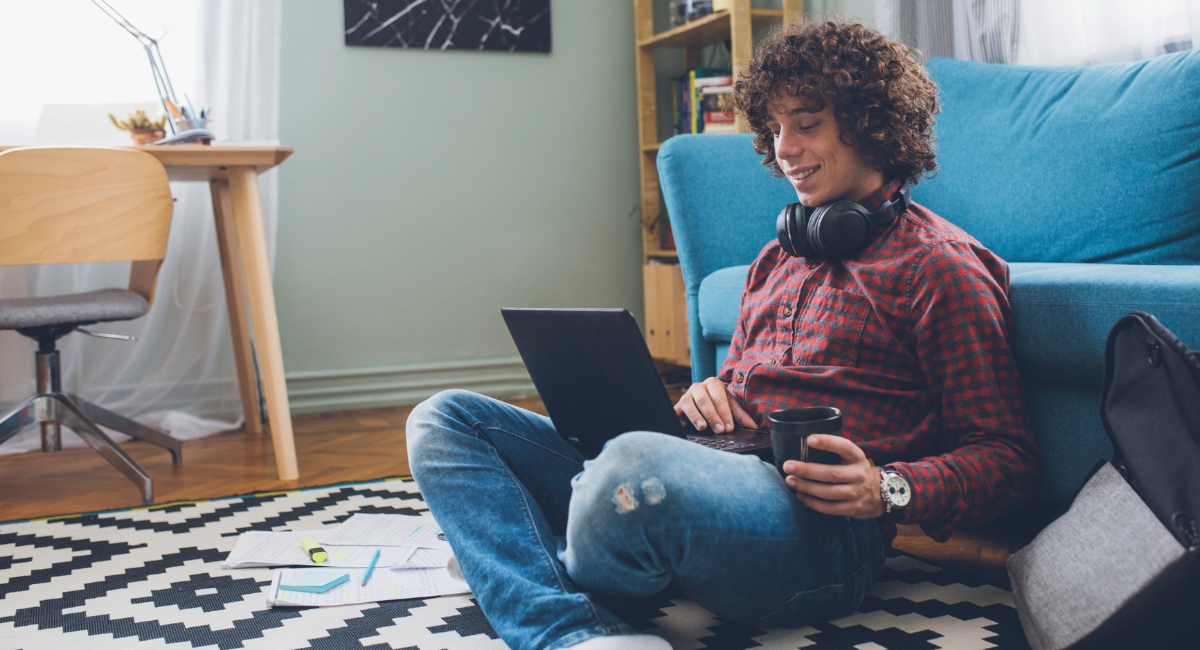 A teen boy sitting and smiling down at his laptop