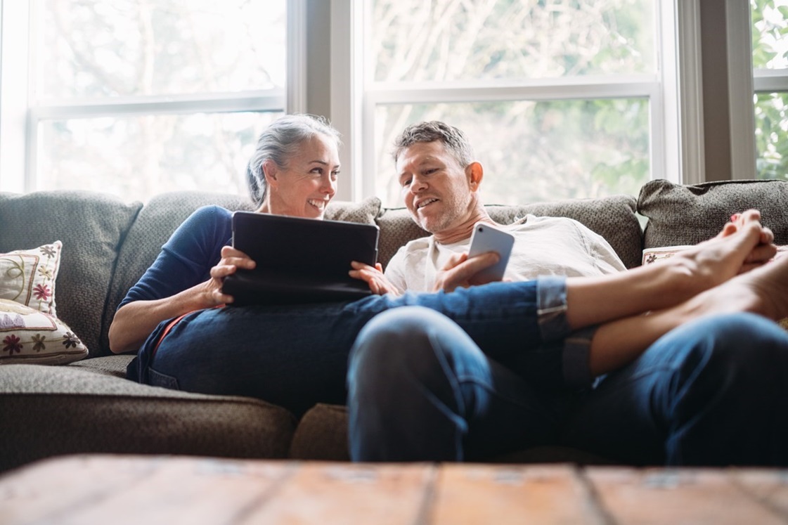 Older man and woman sitting on couch, looking at laptop
