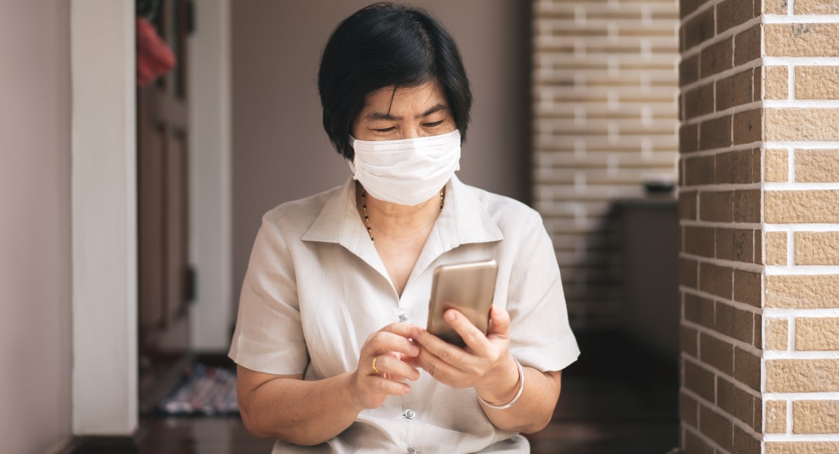 Older woman wearing facemask, looking at phone screen
