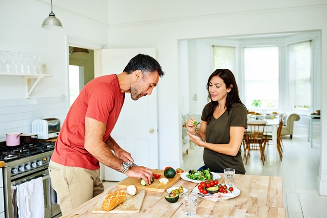 Man and woman preparing healthy sandwiches and salad at a kitchen bench