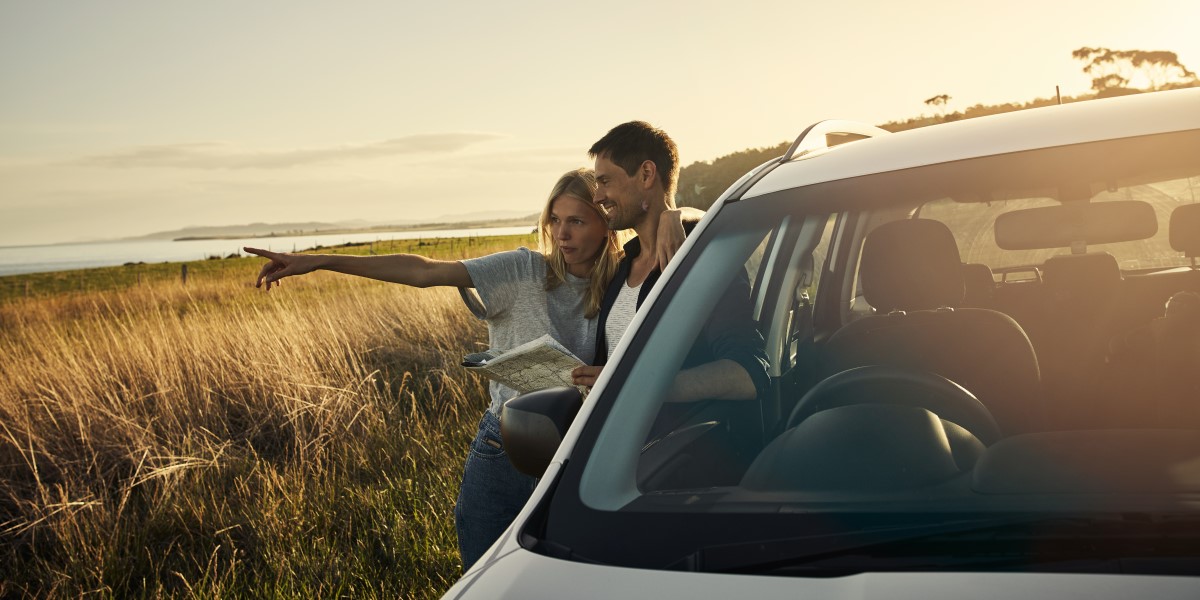 Happy man and woman looking out their car, woman pointing off into the distance
