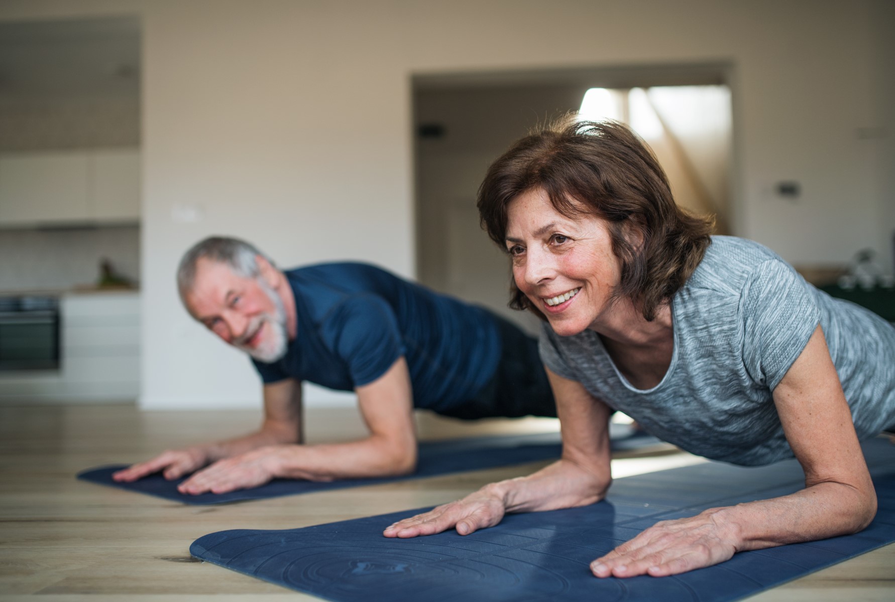 Older man and woman planking on the floor of their home.