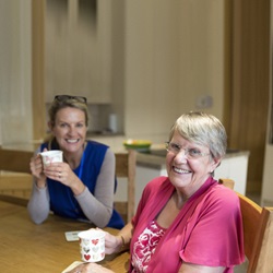 Smiling care worker with smiling customer, who are both drinking a cup of tea