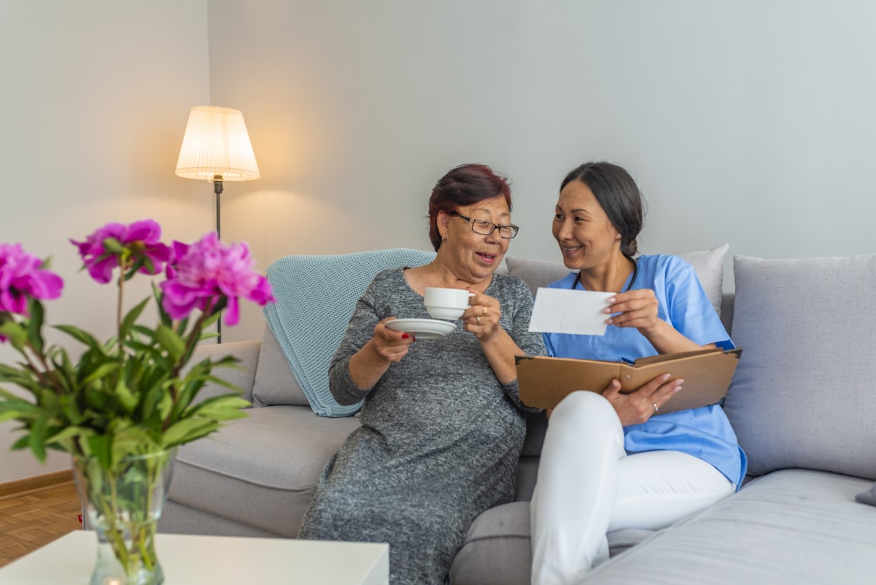 Smiling care worker looking at photo album with smiling customer, who is drinking a cup of tea