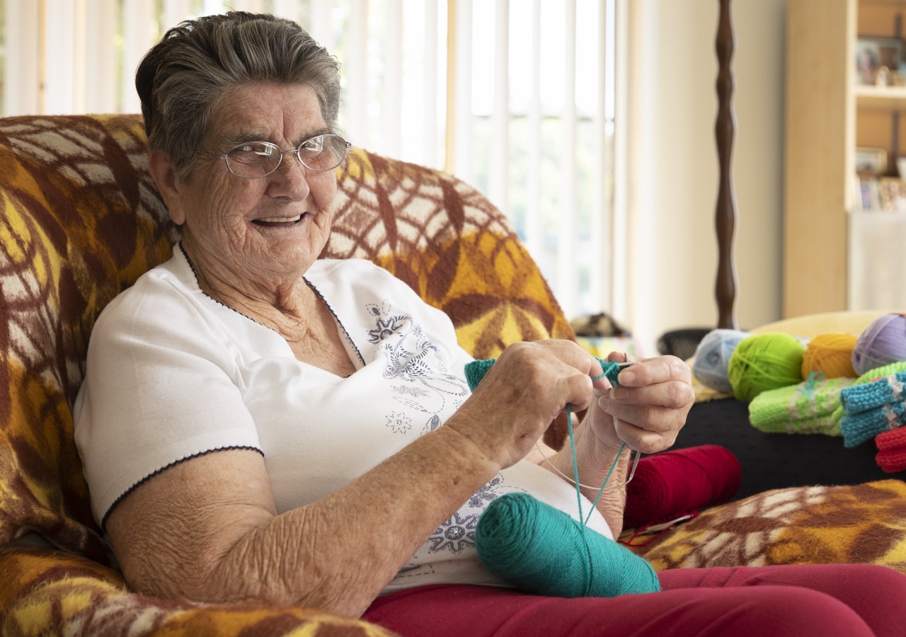 Norma Lindsay sitting in an armchair and knitting