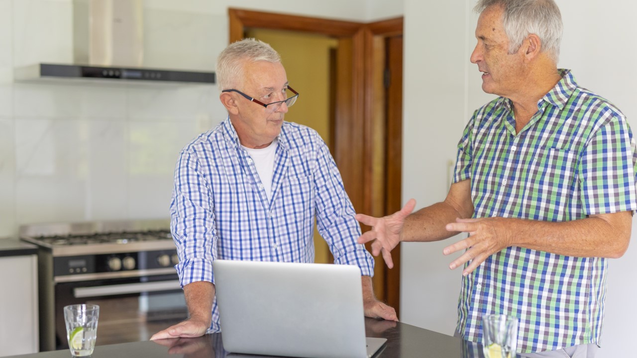 Two men talking and looking at laptop on kitchen bench