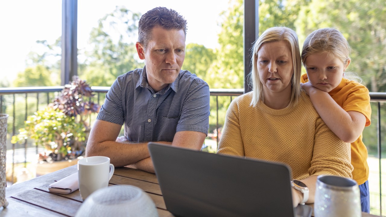 Man and woman looking at laptop, with child also looking over woman's shoulder
