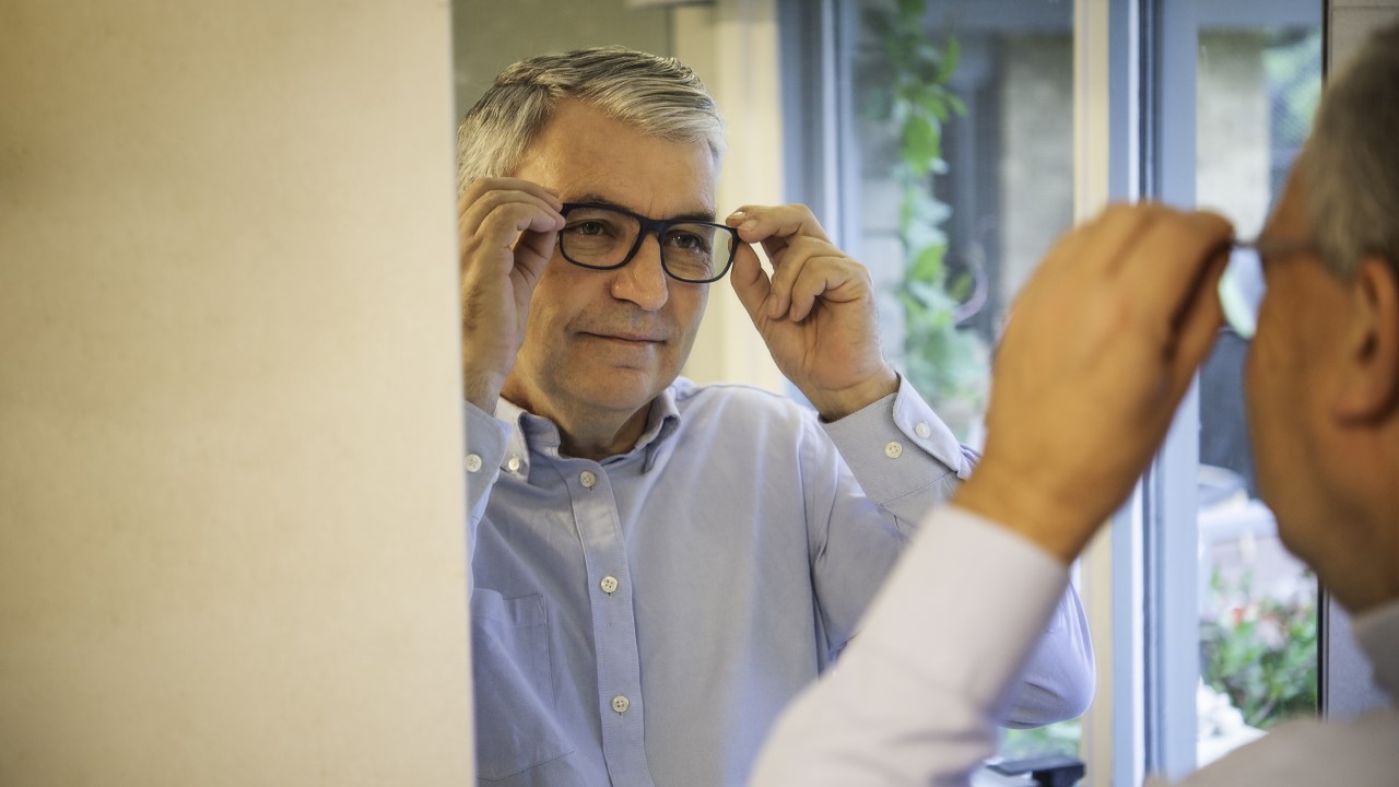 Older man wearing glasses looking at his reflection in the mirror