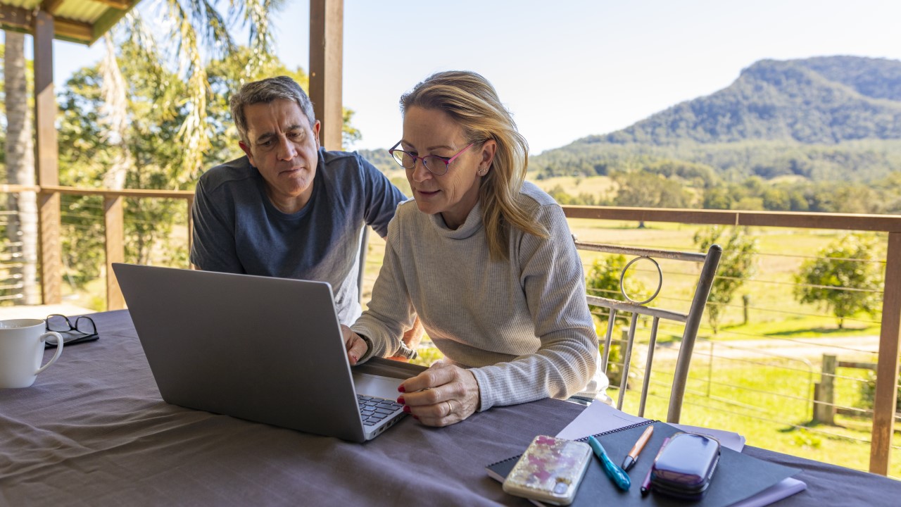 Man and woman looking at laptop, sitting on outside deck.