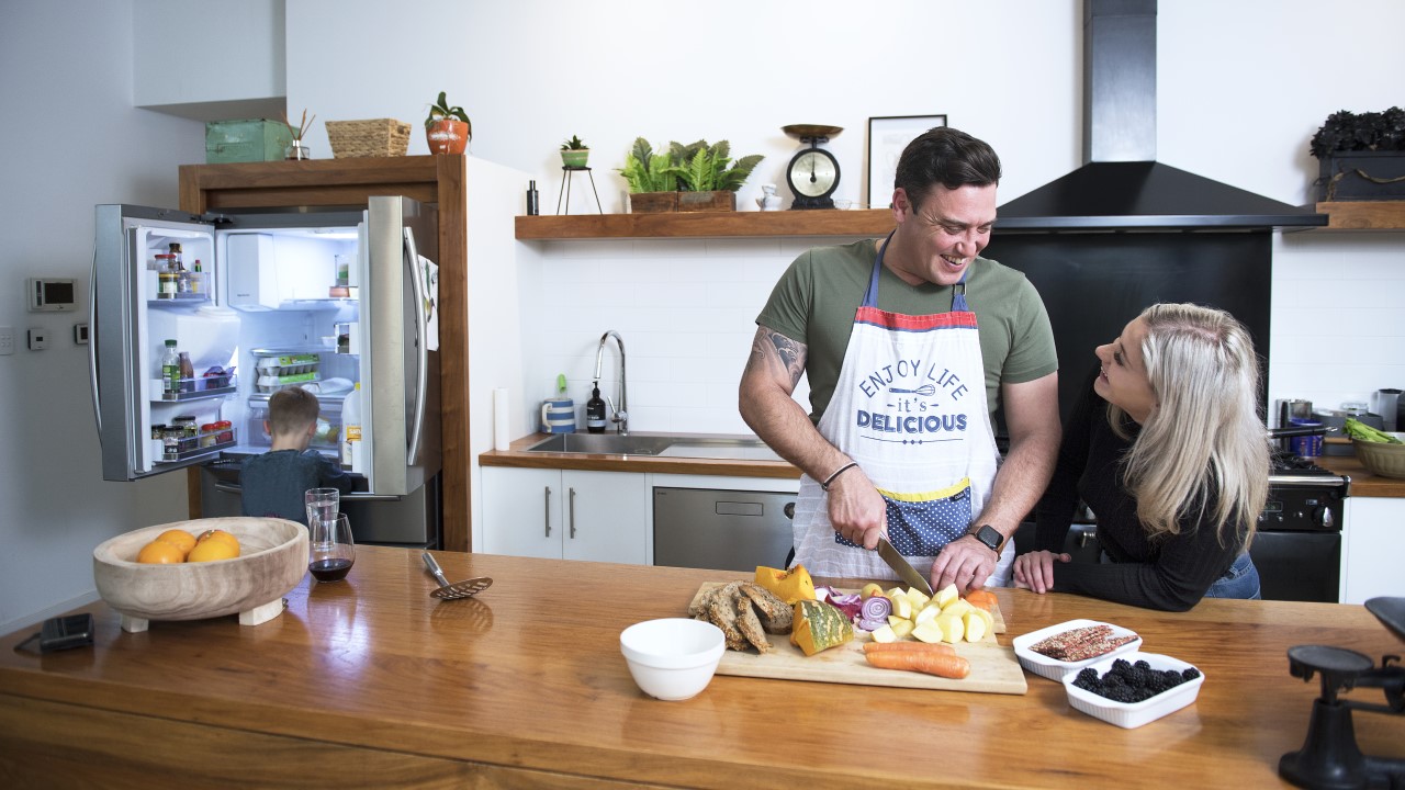 Man and woman talking in kitchen, child looking in fridge