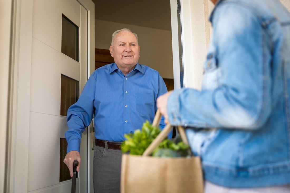 Older man receiving groceries at his front door while maintaining social distancing.