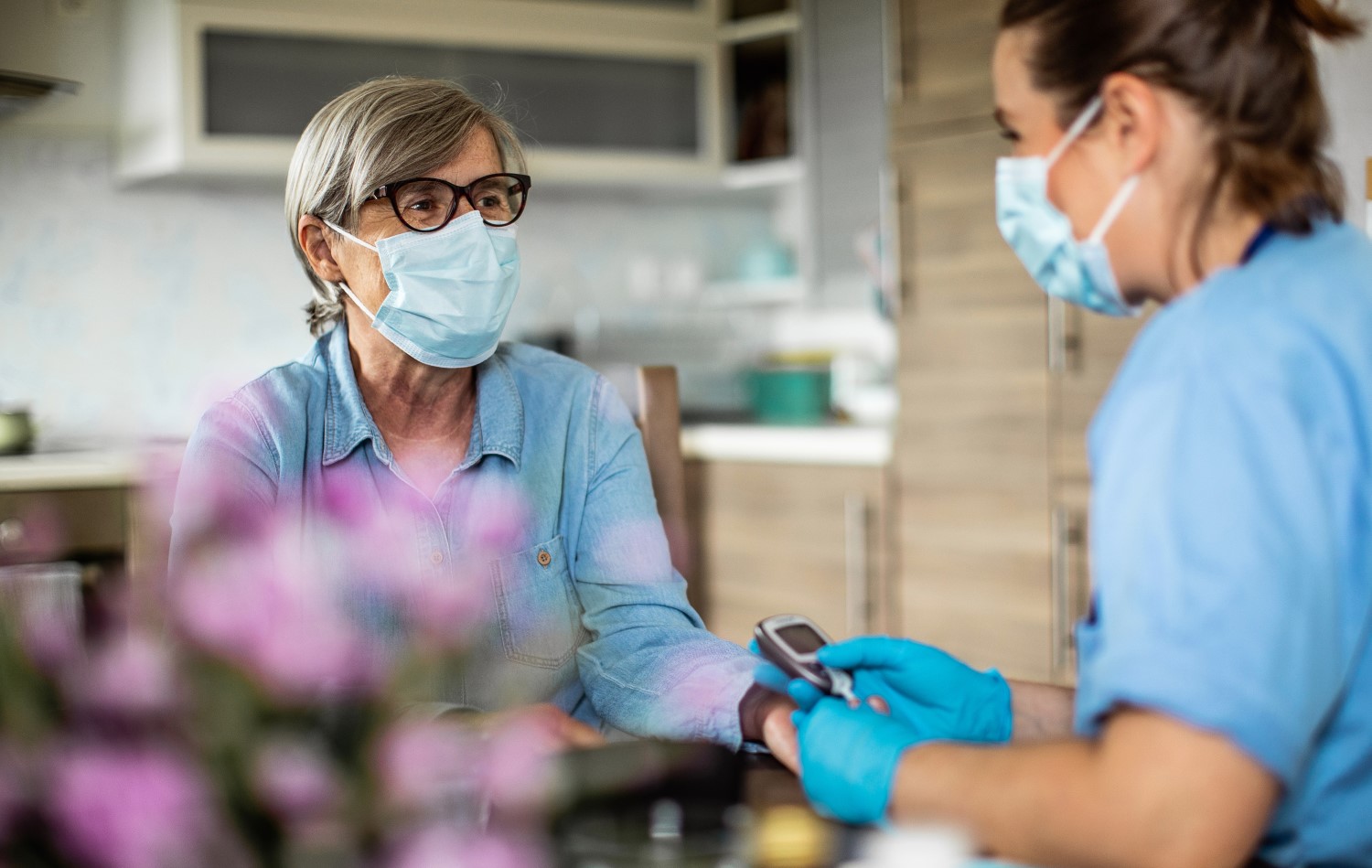 Older woman in surgical mask getting blood pressure check from nurse also wearing surgical mask