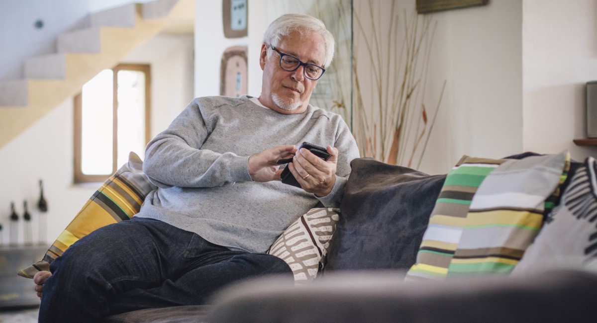 Older man sitting on couch looking at phone screen