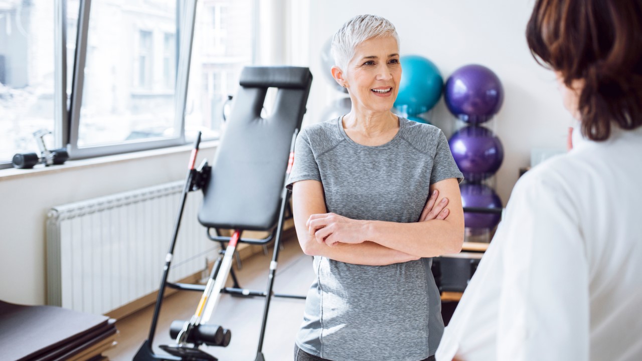 Older woman, arms crossed, listening to physiotherapist