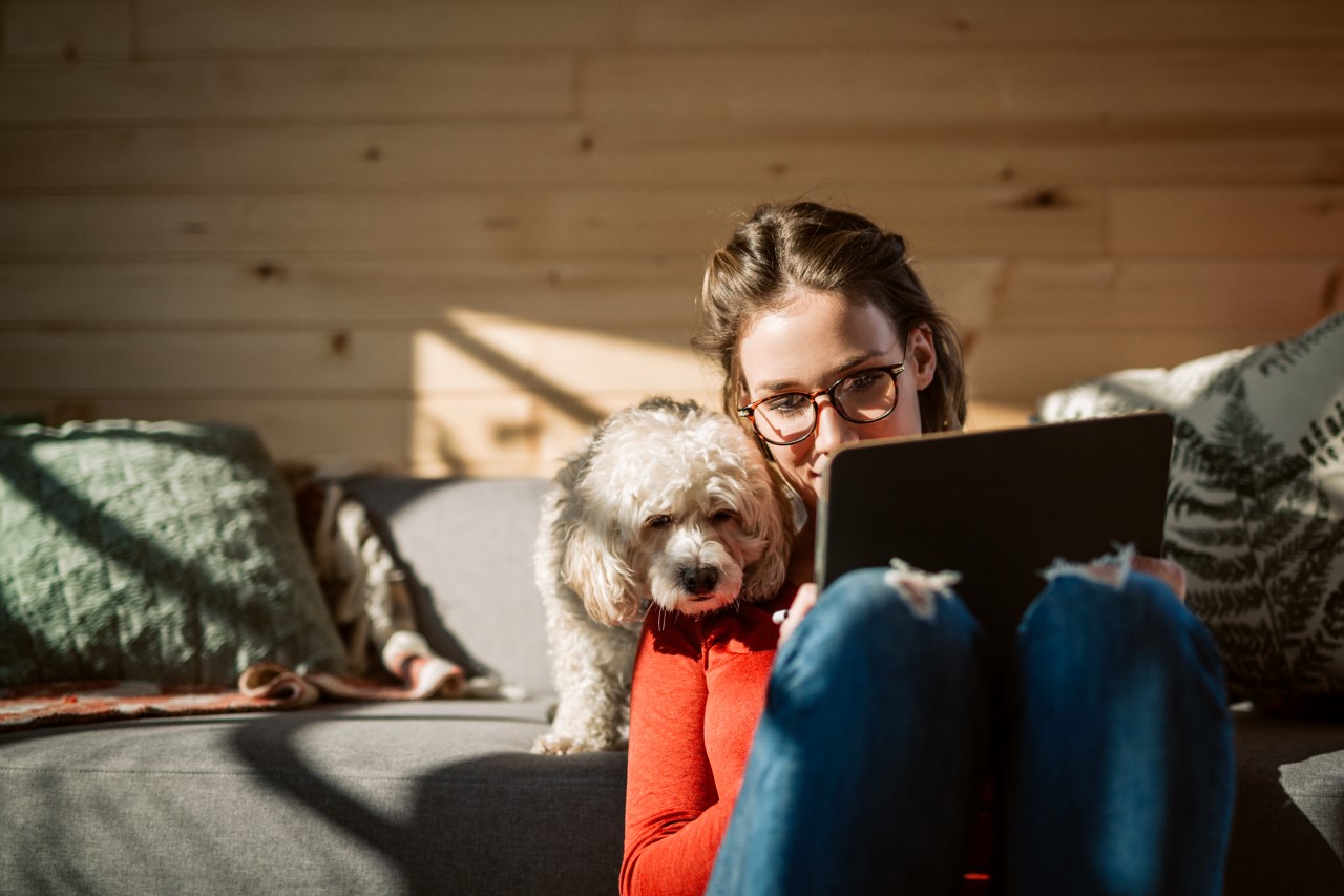 Woman in glasses looking at ipad with small terrier dog looking over her shoulder.
