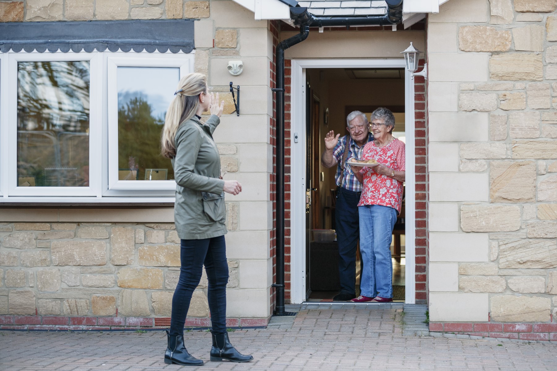 Woman maintaining social distancing from elderly couple in doorway