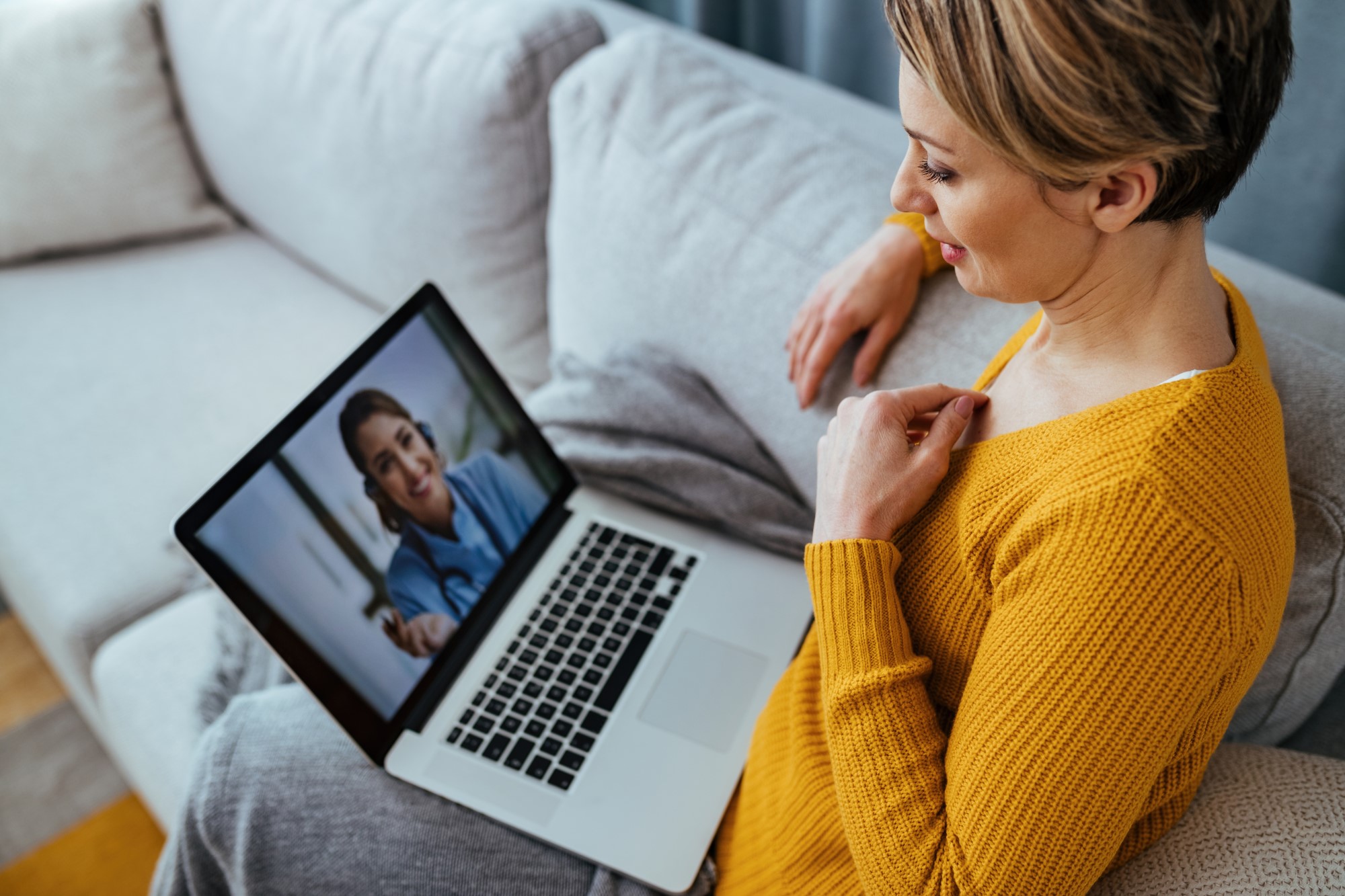 Woman sitting on couch, looking at telehealth appointment on laptop