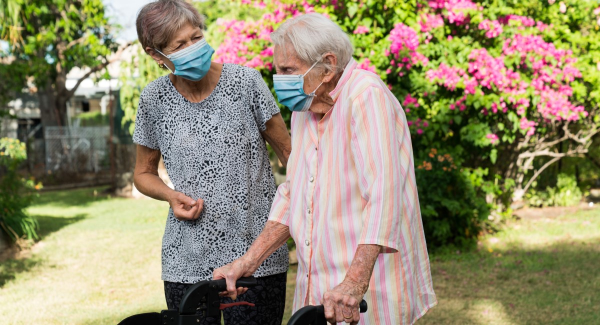 Care worker helping elderly woman who is walking with a mobility frame