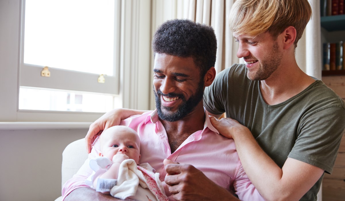 Dad and partner smiling and holding their baby