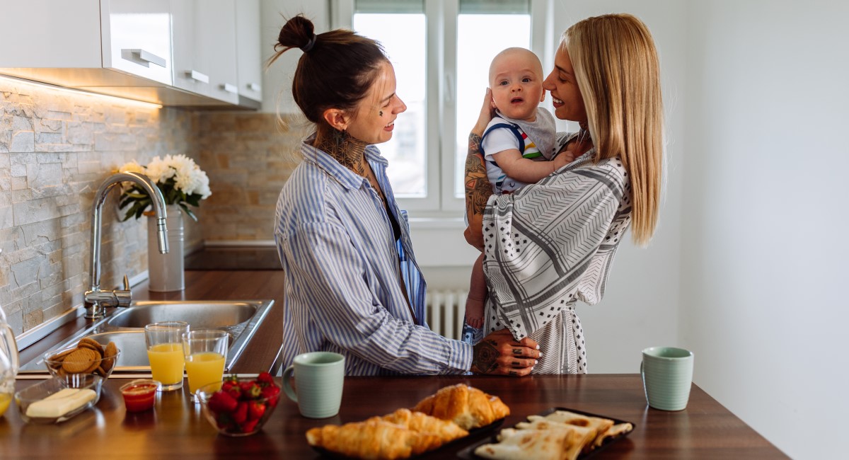 Mum and partner smiling and holding their baby