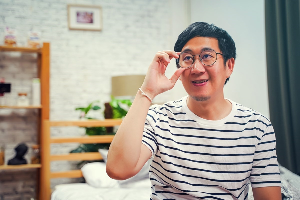 Man in striped t-shirt adjusting the frames of his glasses