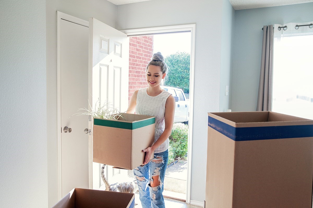 Smiling woman carrying a box into her new home