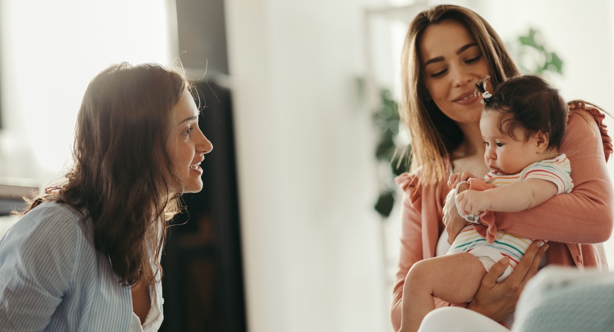 Woman holding her baby laughing and smiling with another woman