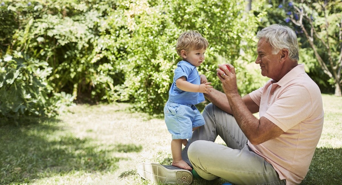 Older man playing with young child in sunny garden
