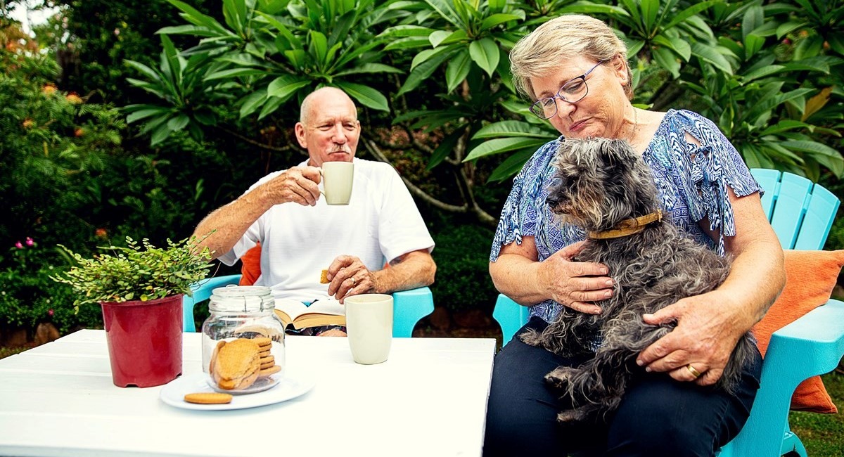 Older man and woman smiling and playing with their dog