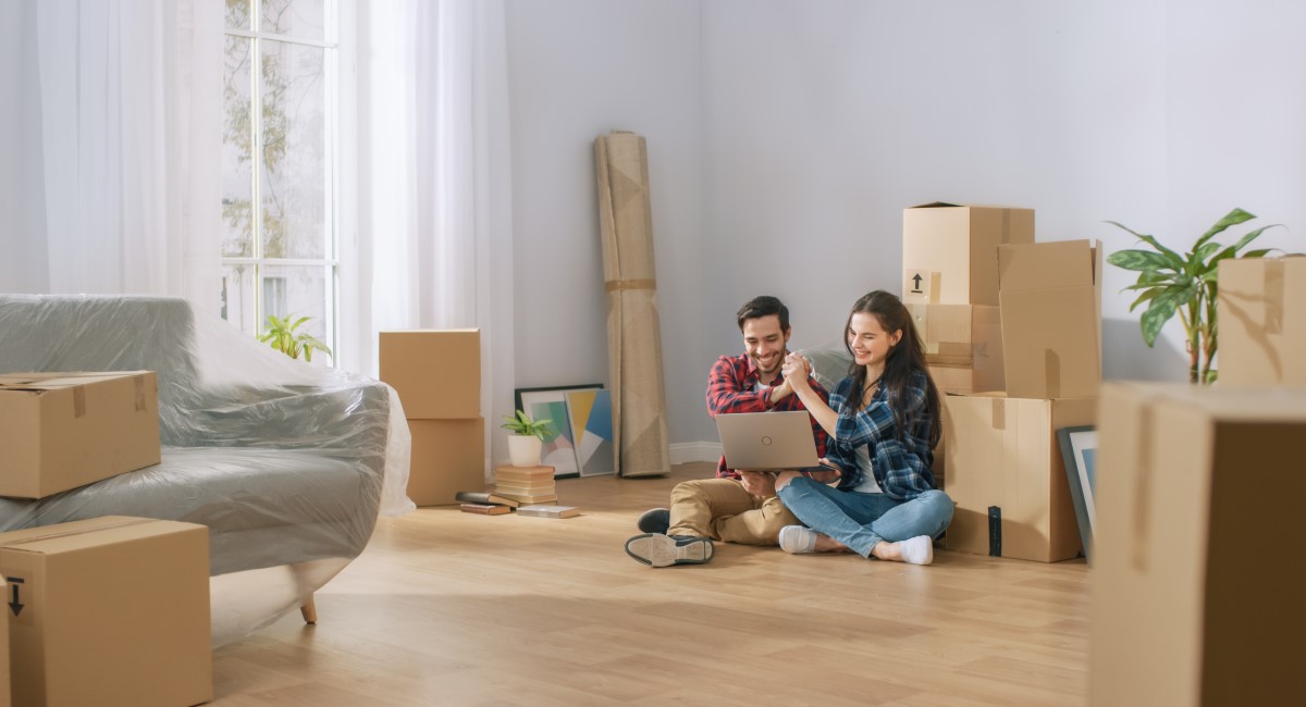 Smiling man and woman sitting on floor, surrounded by moving boxes