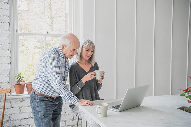 Older man and woman standing at kitchen bench, looking at laptop screen
