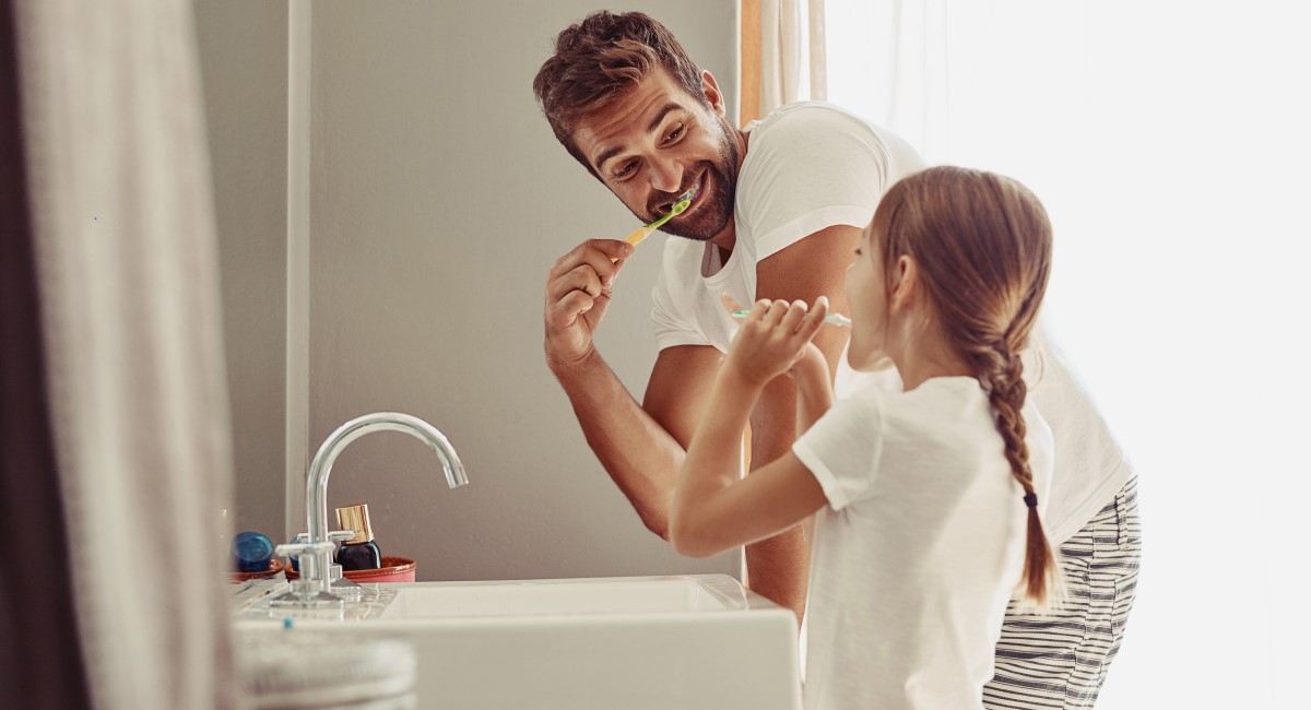 Dad brushing teeth with young daughter