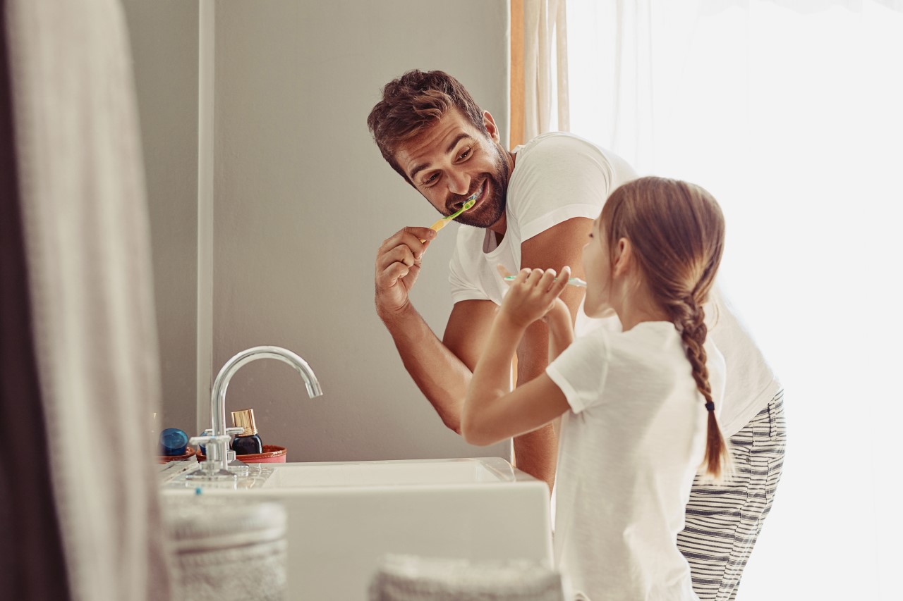 Happy smiling father and young daughter brushing their teeth in front of bathroom sink