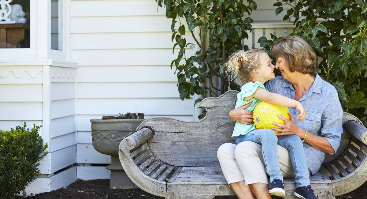 Smiling grandmother nose to nose with smiling grand-daughter on a couch outside