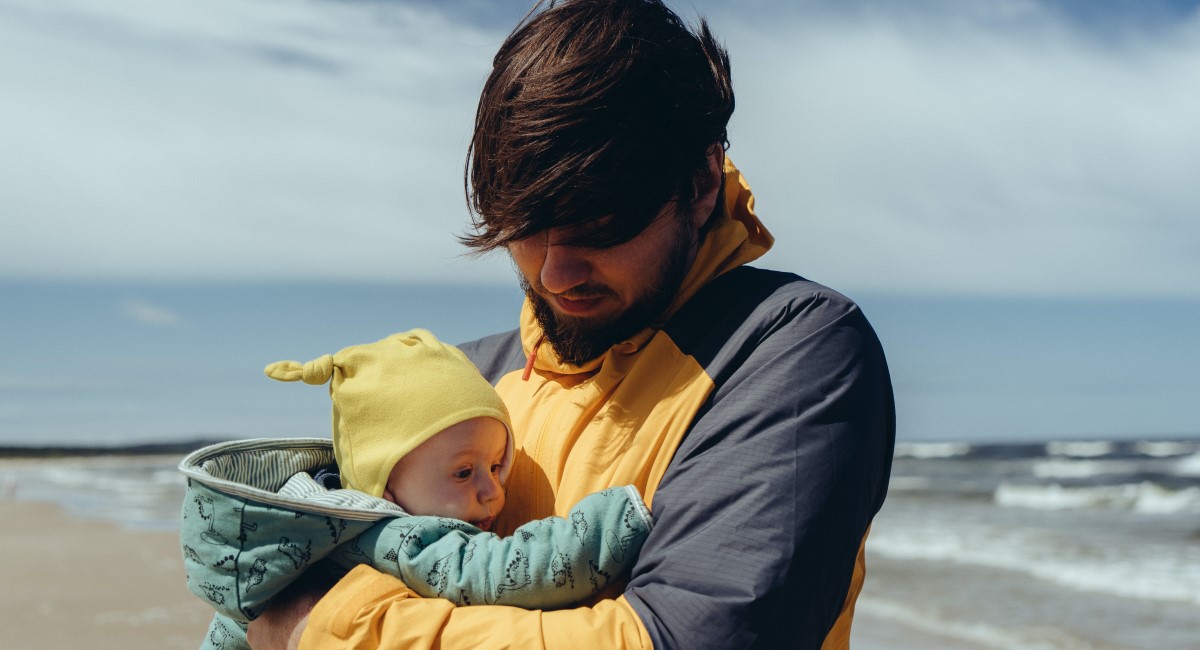 Dad with baby strapped to chest walking along the beach