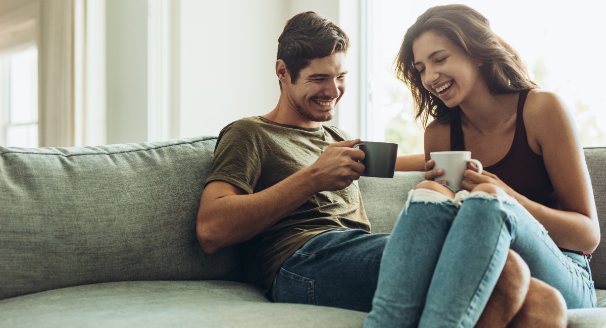 Man and woman sitting on couch laughing and enjoying coffee