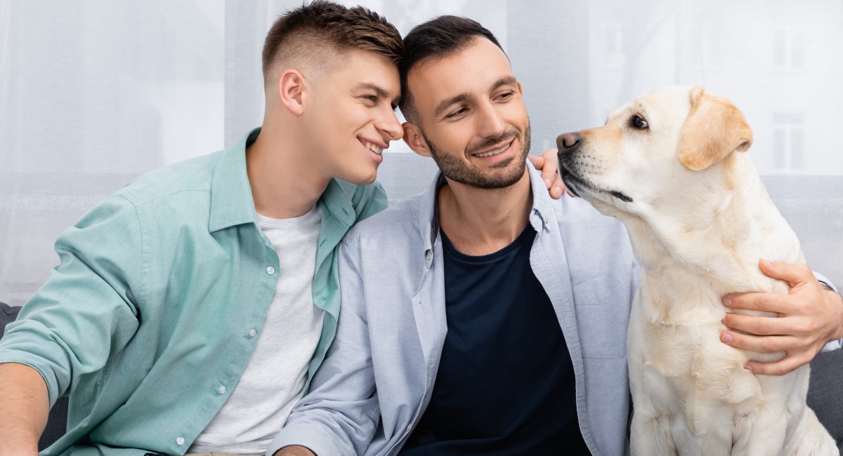 Two men smiling and looking at their yellow labrador