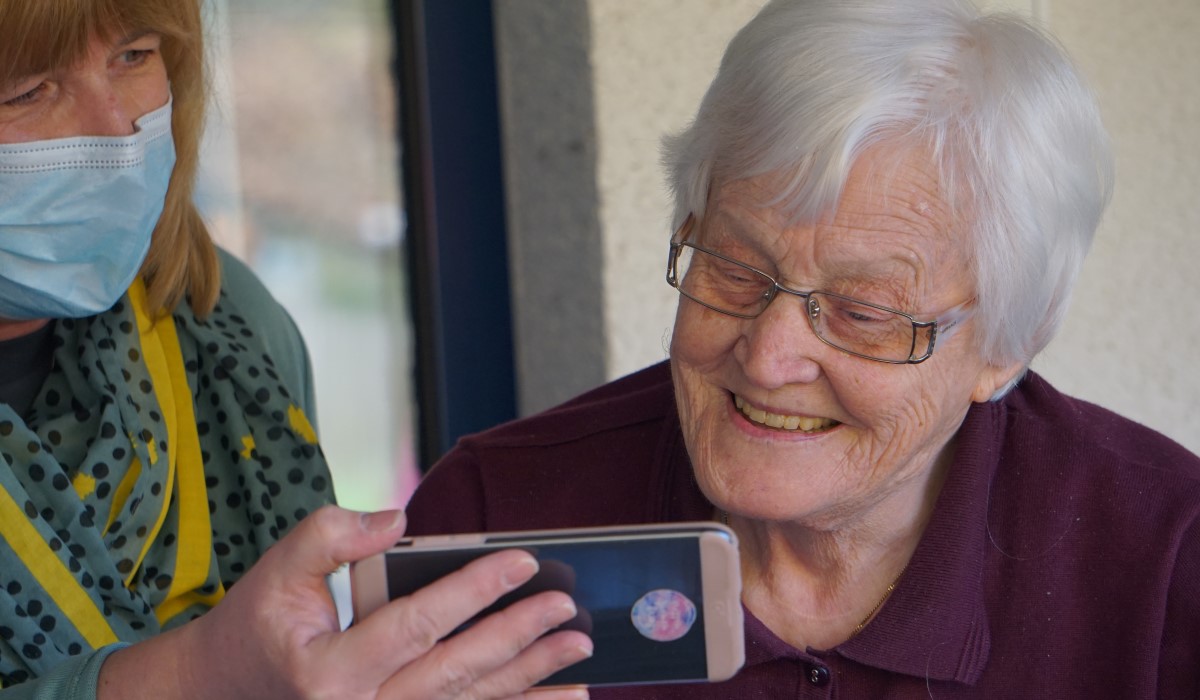 Older woman looking at phone screen with care worker