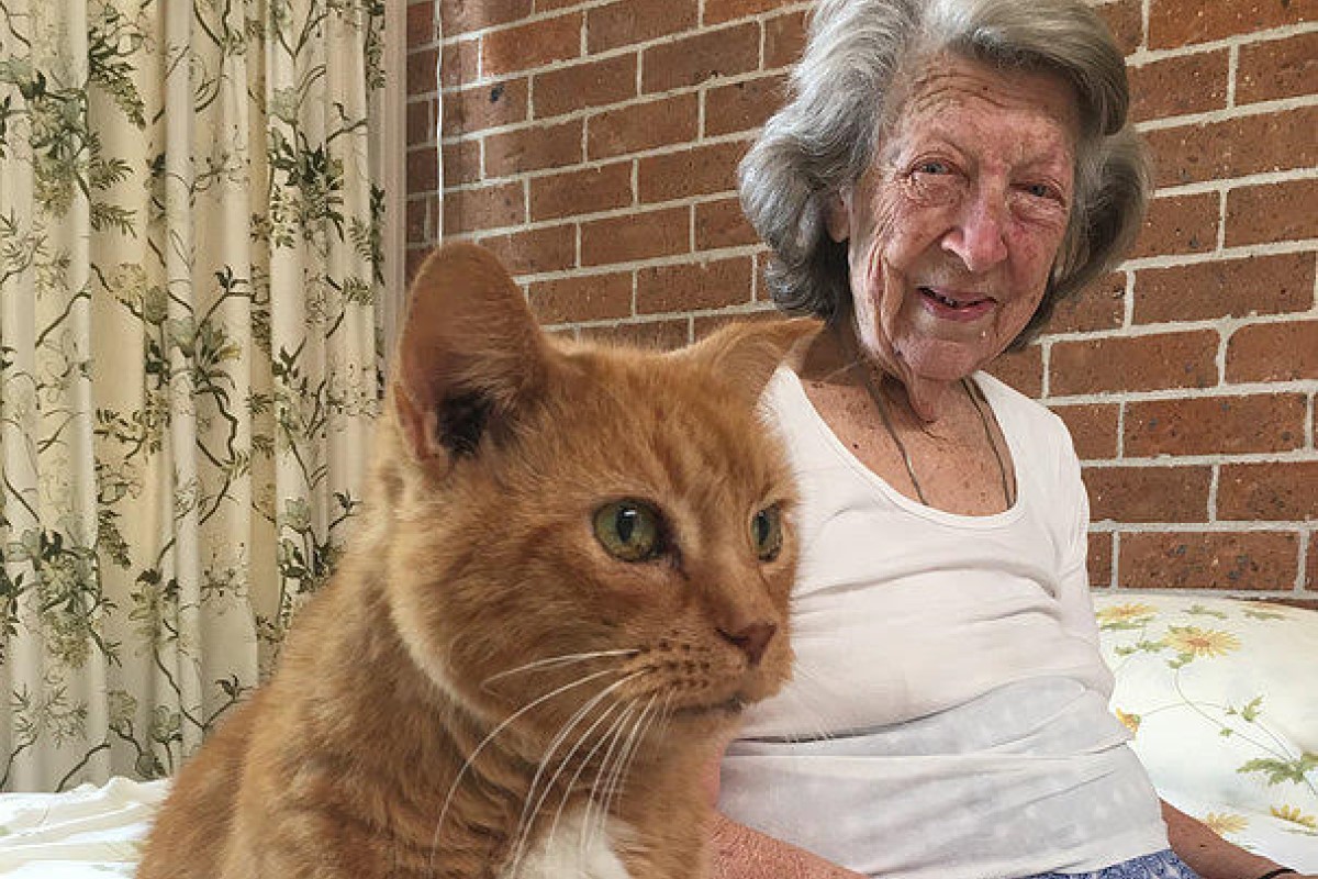 Australian Unity customer Patricia Hannan and her cat Chum sit comfortably together on the bed.