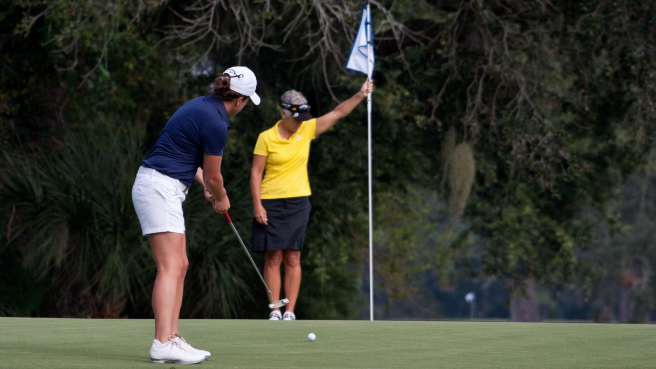 woman putting on a golf green, another woman holding the flag near the hole
