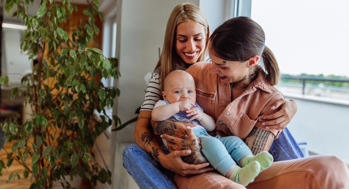 Mum and partner smiling and holding their baby