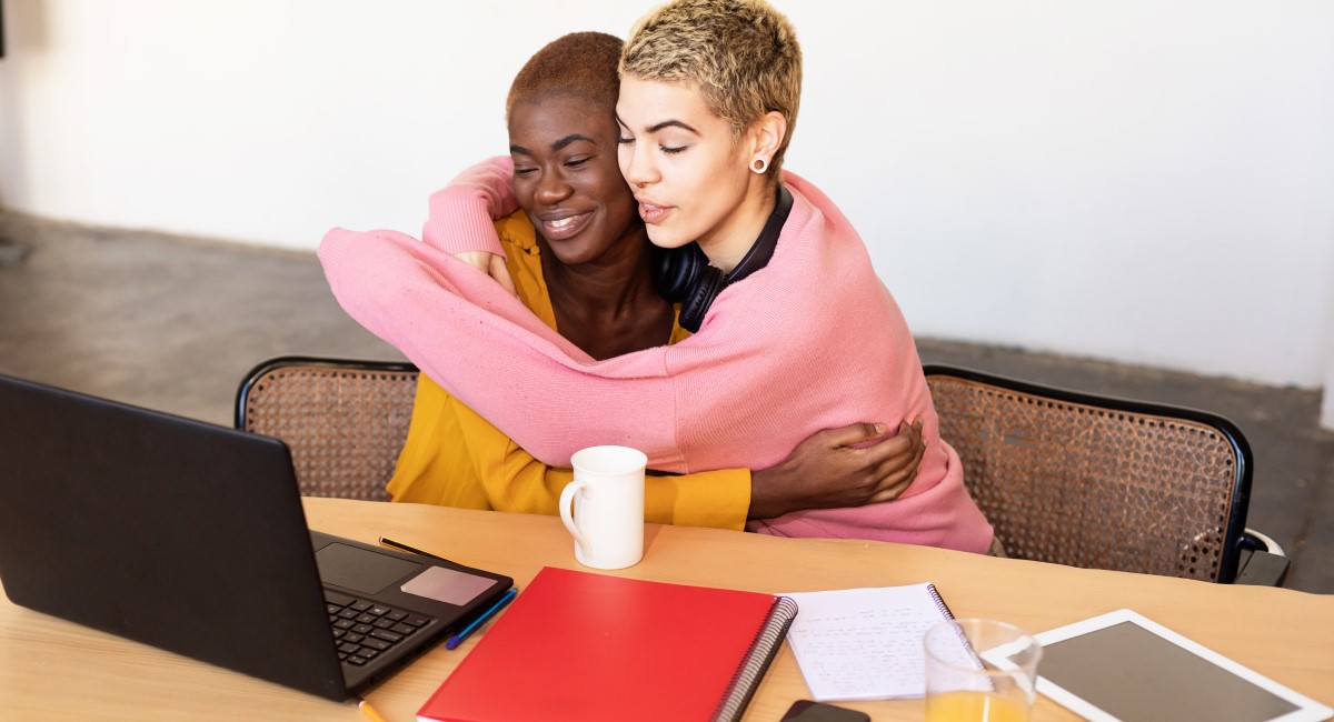 Two women hugging while looking at a laptop